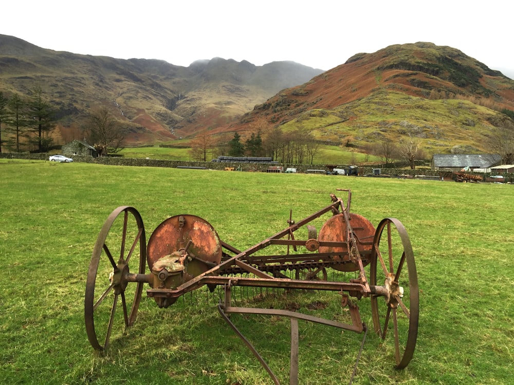 a rusted metal plow in a field with mountains in the background