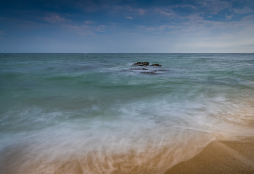 a beach with a rock in the middle of the ocean