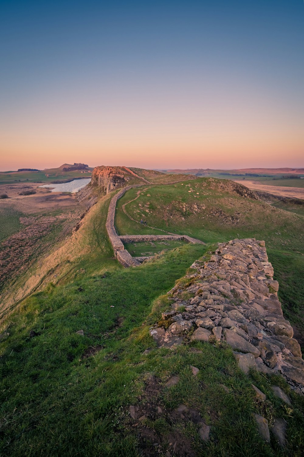 a stone wall on a grassy hill with a river in the distance