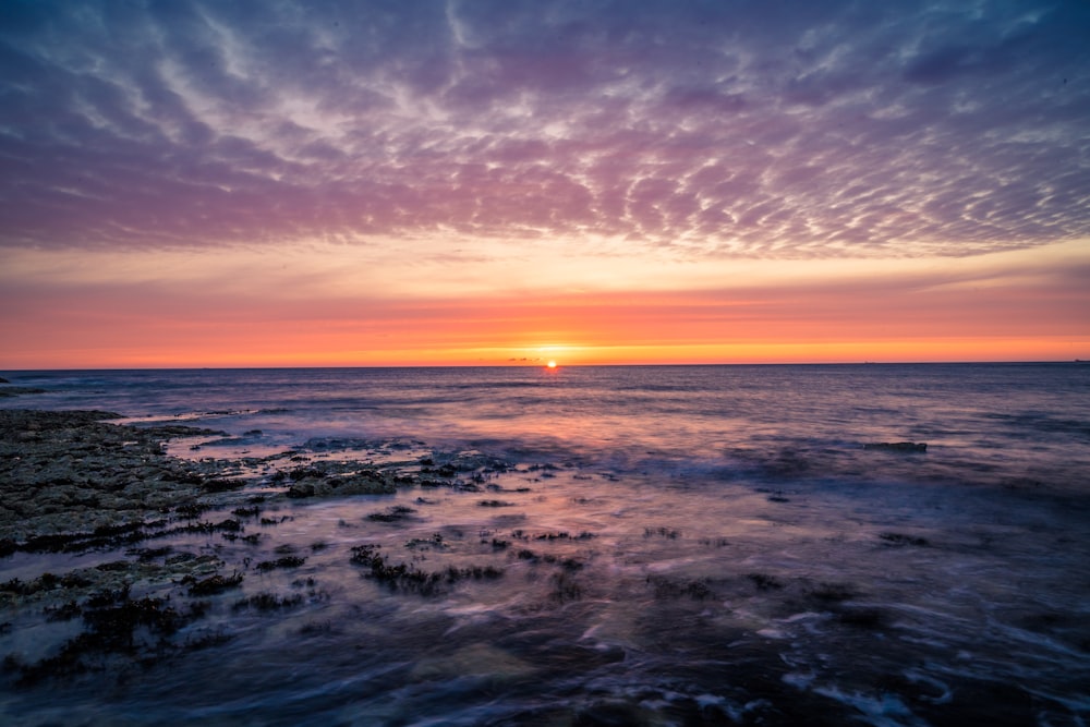 the sun is setting over the ocean on a cloudy day