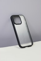 A smartphone case with a sleek, semi-transparent back featuring curvy line patterns. The case has a black border and is displayed against a plain, grayish wall with a white surface at the bottom.