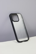 A smartphone case with a sleek, semi-transparent back featuring curvy line patterns. The case has a black border and is displayed against a plain, grayish wall with a white surface at the bottom.