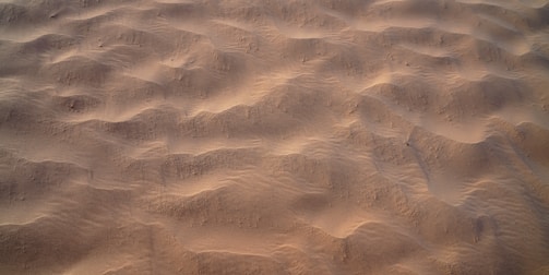 Rough surface of desert sand dunes with subtle ripples and shadows, showing natural patterns created by the wind.
