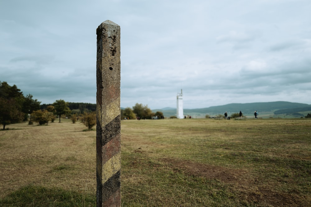 a pole in a field with a lighthouse in the background