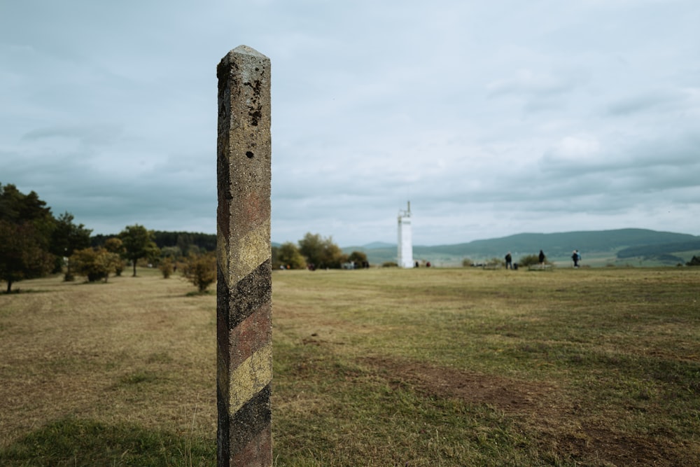 ein Pfahl auf einem Feld mit einem Leuchtturm im Hintergrund