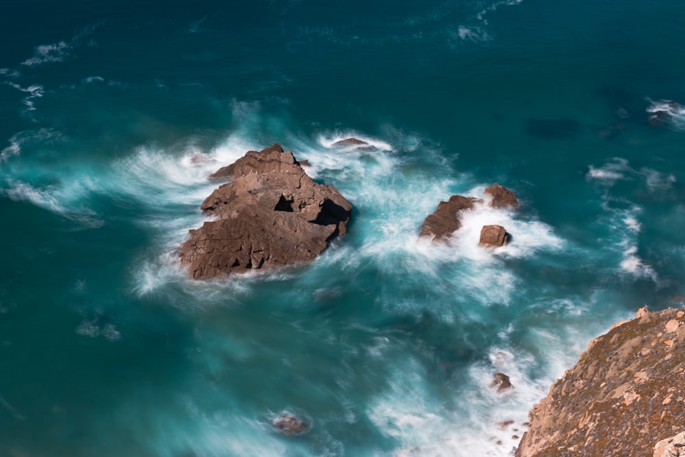 an aerial view of the ocean with rocks in the foreground