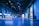 An indoor exhibition hall with high ceilings lit in blue lighting. Several informational booths line the sides, with a prominent booth labeled 'HSLU' in the foreground. People are walking and interacting throughout the space, creating a lively atmosphere.
