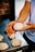 A person holding a perfectly shaped dough ball in their hands, with several other dough balls resting on a metal surface in the background. The setting appears to be a bakery or kitchen, with warm lighting enhancing the texture of the dough.