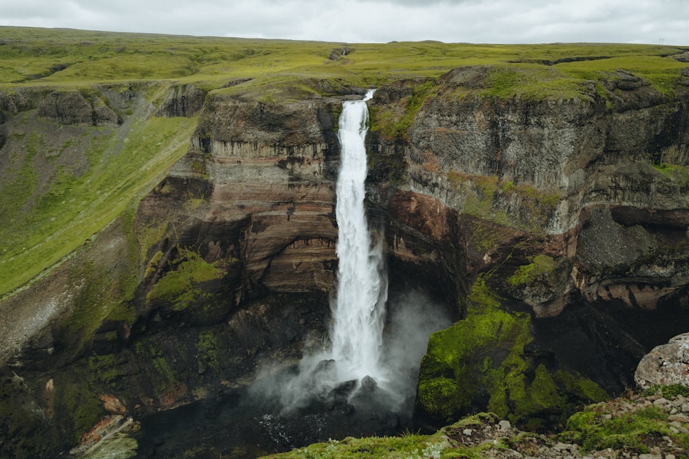 una cascada con un campo verde al fondo