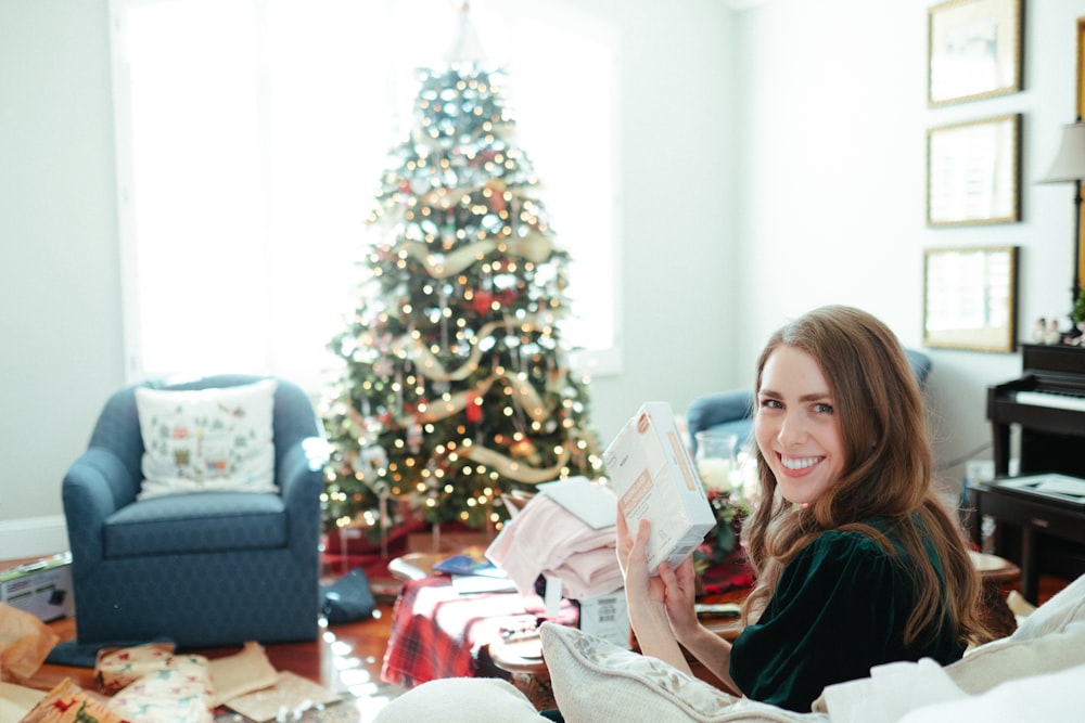 a woman sitting on a couch in front of a christmas tree