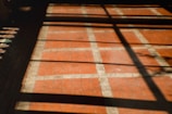A tiled floor with a red and white grid pattern is partially covered by shadows cast from a window, forming rectangular shapes on the surface.