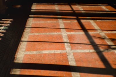 A tiled floor with a red and white grid pattern is partially covered by shadows cast from a window, forming rectangular shapes on the surface.