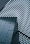 An abstract architectural design featuring intersecting lines of a modern building. The structure is composed of sleek, reflective glass panels and diagonally aligned metallic siding, creating a striking geometric pattern.