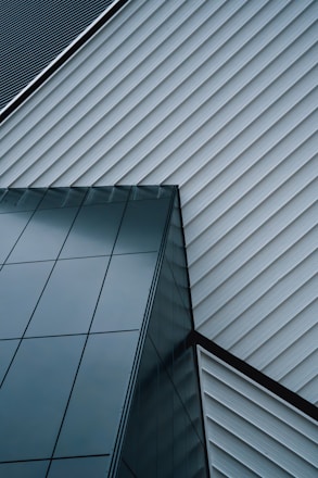 An abstract architectural design featuring intersecting lines of a modern building. The structure is composed of sleek, reflective glass panels and diagonally aligned metallic siding, creating a striking geometric pattern.