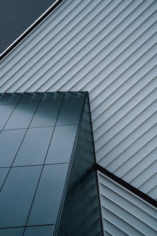 An abstract architectural design featuring intersecting lines of a modern building. The structure is composed of sleek, reflective glass panels and diagonally aligned metallic siding, creating a striking geometric pattern.