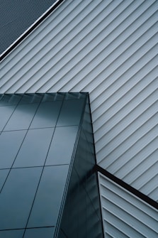 An abstract architectural design featuring intersecting lines of a modern building. The structure is composed of sleek, reflective glass panels and diagonally aligned metallic siding, creating a striking geometric pattern.