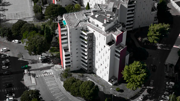 An aerial view of a multi-family residential building showcasing its symmetrical layout and landscaped surroundings on a bright sunny day.