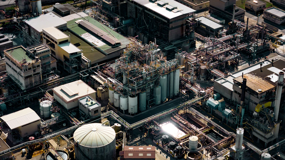 A panoramic view of an industrial oil and gas facility at sunset, highlighting complex pipelines and machinery.