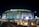 A large, illuminated stadium at night with bright signage including the MetLife and HCLTech logos. People are walking towards the entrance, and the surroundings are well-lit, with barriers guiding pedestrian traffic.