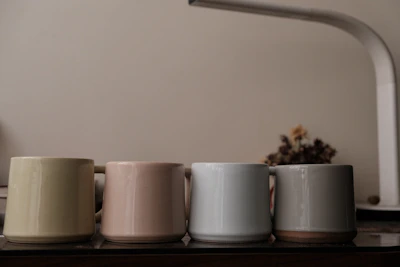 Close-up of matte forest green ceramic mugs stacked neatly on a parchment-colored countertop, highlighting their smooth texture.