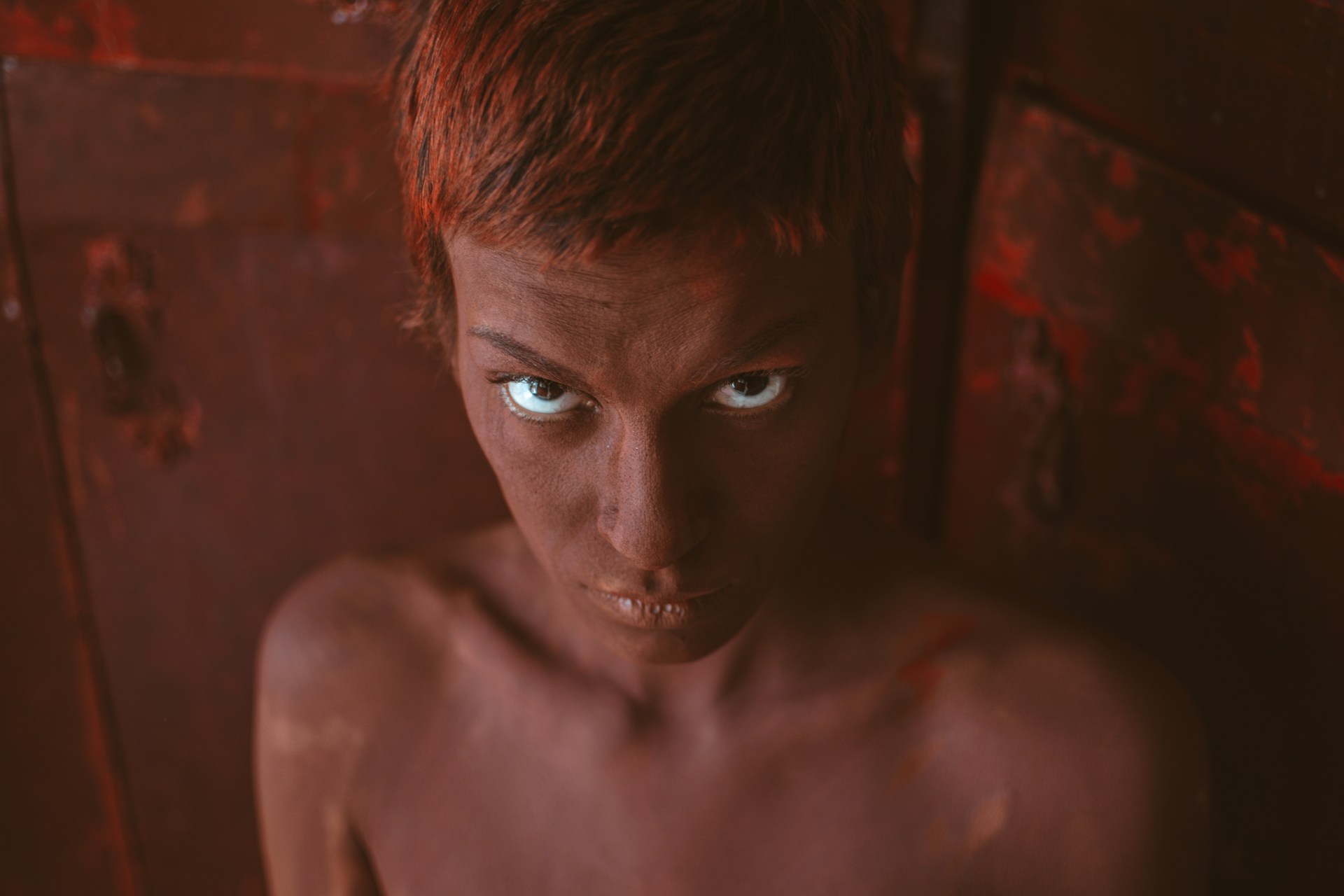 A close-up of Ilker Karacam with intense expression, bathed in moody dark tones with vibrant red highlights.