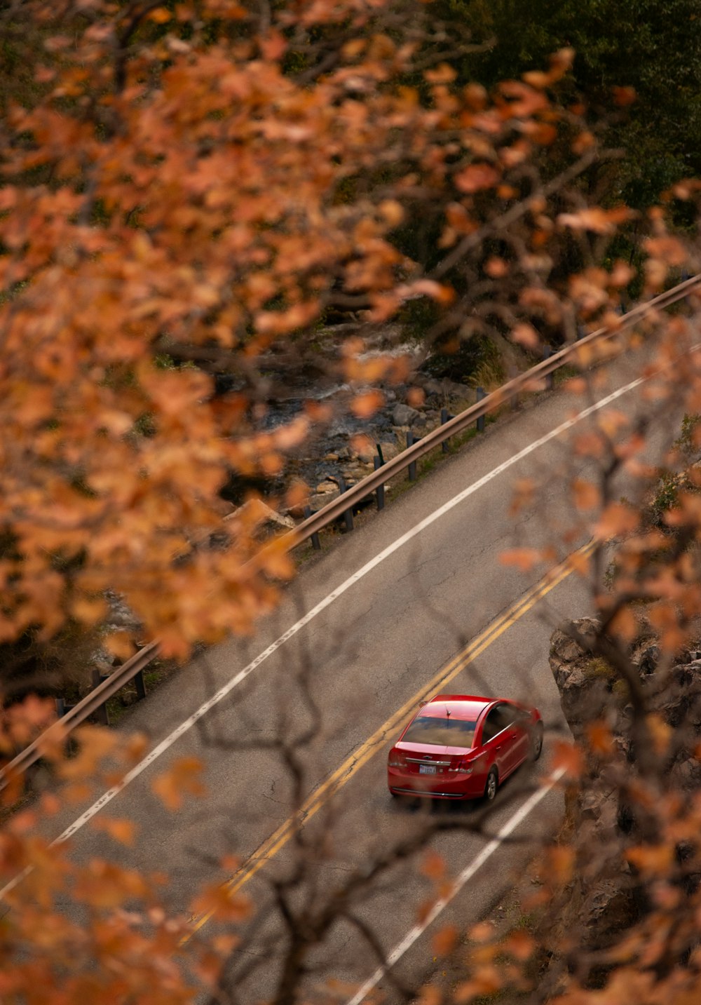 a red car driving down a road next to a forest