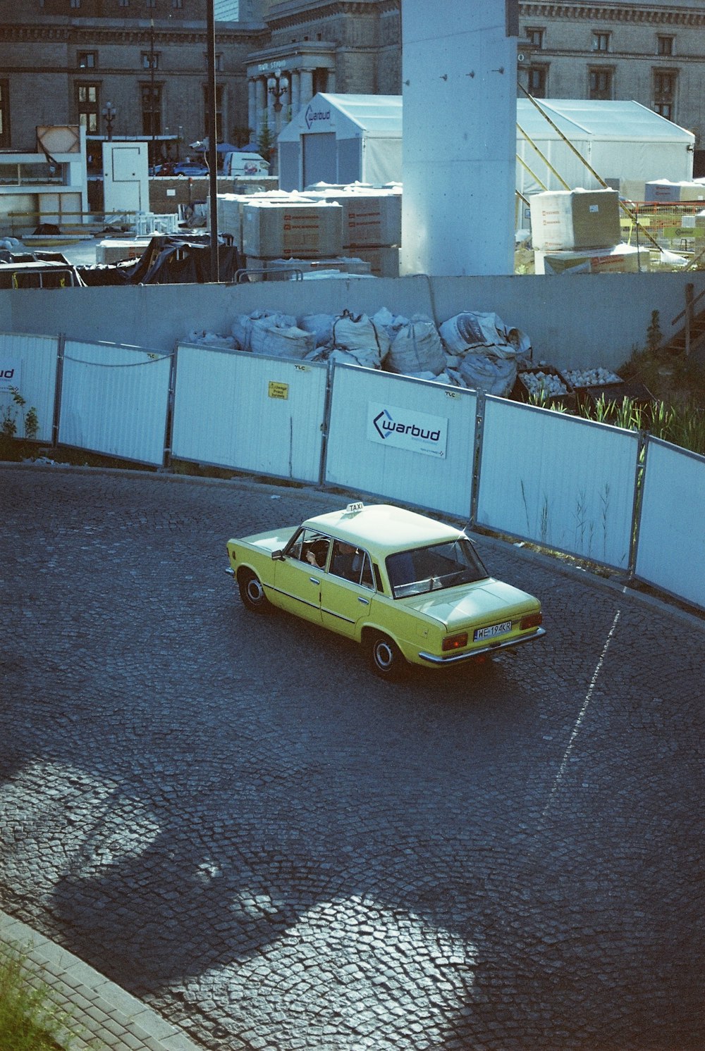 a yellow car driving down a street next to a tall building