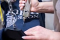 A person is pressing a metallic tool onto a dark blue cloth, possibly involved in printing or embroidery. The cloth features white text and a graphic design. The person’s hands are visible, and they have white nail polish.