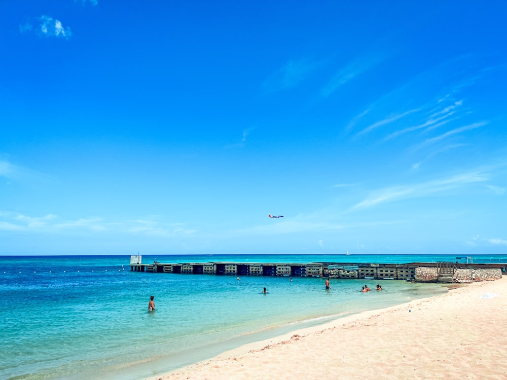 a beach with people swimming and a plane flying in the sky