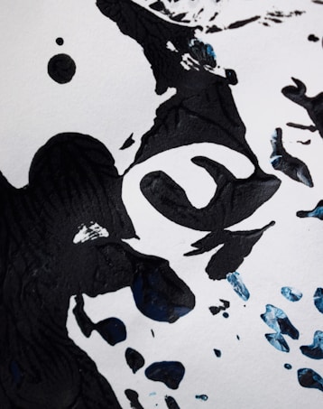 Abstract black ink shapes on a white background, with a few splashes of blue ink scattered around. The arrangement of the ink suggests a modern art piece with fluid forms and bold contrasts.