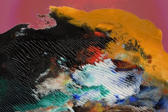 An abstract, textured artwork featuring a blend of vibrant colors with swirling patterns and ridges. The central area shows a dynamic mix of white, blue, and green shades, surrounded by darker tones of black and teal. The upper section includes bold patches of yellow and orange with intricate textures.
