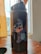 A dark-colored water bottle with a cheerful cartoon character printed on it, placed on a wooden surface near a window with light curtains.