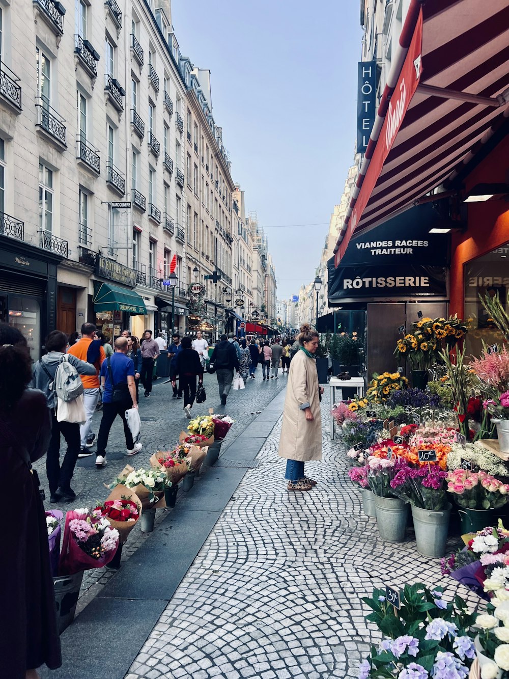a woman walking down a street next to a bunch of flowers
