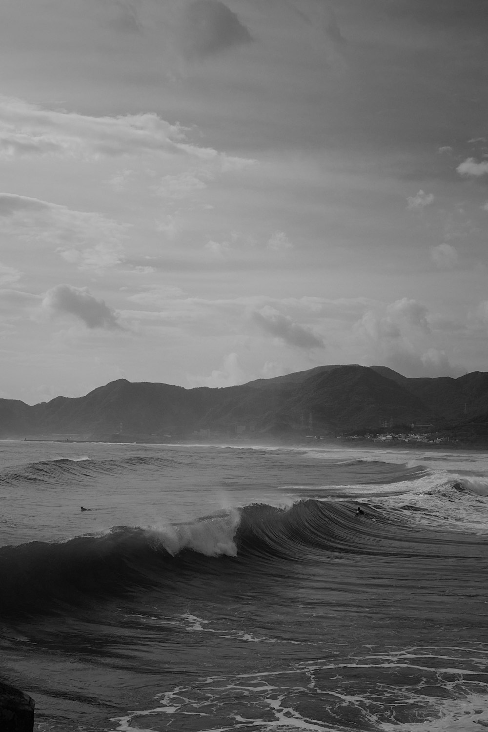 a black and white photo of the ocean with mountains in the background