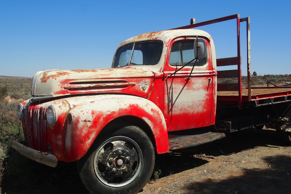 an old red truck parked on a dirt road