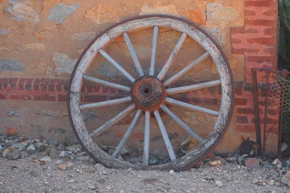 an old wagon wheel leaning against a brick wall