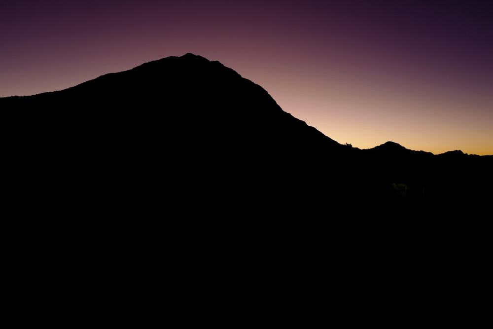 the silhouette of a mountain against a purple sky