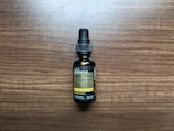A small brown bottle with a black dropper cap labeled as a full spectrum hemp extract, specifically CBD and THC tincture. The label includes the dosage information as 50 mg per serving with 2.5 mg of THC per serving, and it mentions lemon ginger flavor. The bottle is placed on a wooden surface.