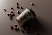 A biodegradable coffee cup with a black lid is tilted on its side on a dark surface. Scattered around the cup are several coffee beans that create a visually appealing arrangement.