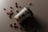 A biodegradable coffee cup with a black lid is tilted on its side on a dark surface. Scattered around the cup are several coffee beans that create a visually appealing arrangement.