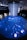 An immersive digital art installation features an illuminated floor with aquatic imagery, including a large digital representation of a marine animal. Several people are interacting with the space, walking on the projection. Above, a cascade of lights or thin strands descends from the ceiling, creating a sense of depth and fluidity in the ambient lighting.