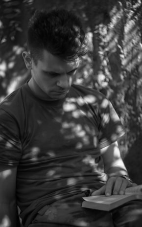 A serene outdoor scene with a reader immersed in a Tenacious Mind Collective book under dappled sunlight.