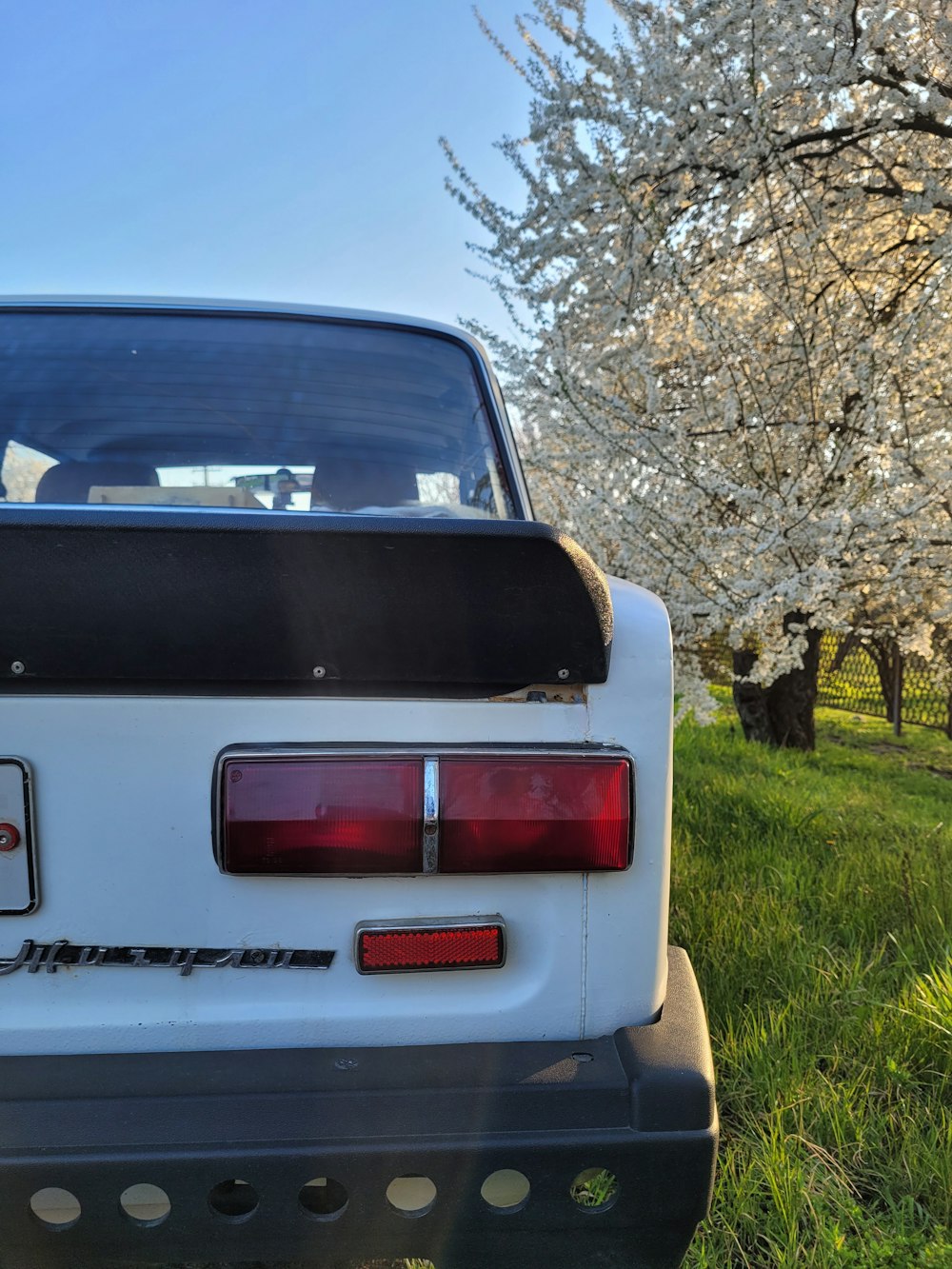 the back end of a white car parked in the grass