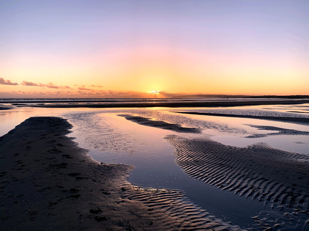 the sun is setting over the water on the beach