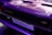 Close-up of a car's rear section, featuring a detailed shot of the badge and tail light area. The surface has a shiny, purple finish with prominent branding visible.