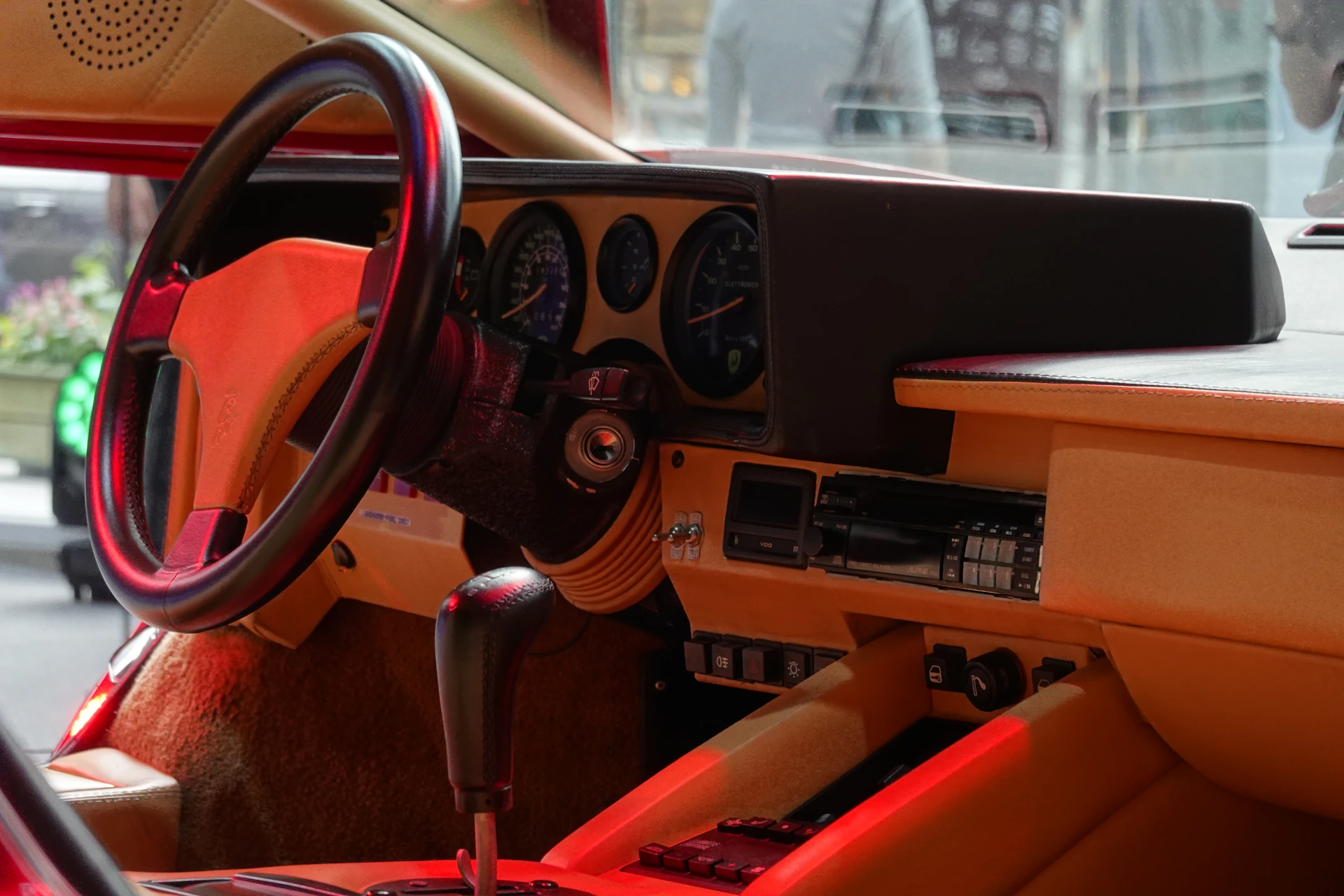 Cozy car interior shot showing a driver adjusting the car radio controls, with parchment-colored upholstery and subtle crimson highlights on the dashboard.