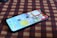 A smartphone is placed on a checkered fabric surface, displaying its home screen with various app icons. The screen features vibrant colors and is slightly tilted, creating a dynamic perspective.