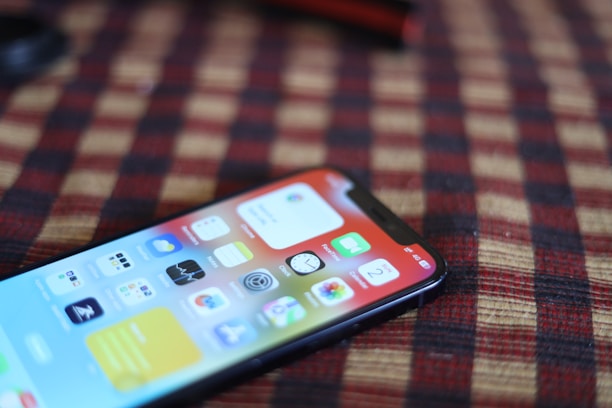 A smartphone with a vivid display showing various app icons lies on a surface with a checkered pattern in red and black. The phone is positioned at an angle, partially in focus.