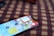 A smartphone with a vivid display showing various app icons lies on a surface with a checkered pattern in red and black. The phone is positioned at an angle, partially in focus.