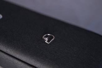 Close-up of a sleek silver ring on a dark textured surface, highlighting its minimalist design.